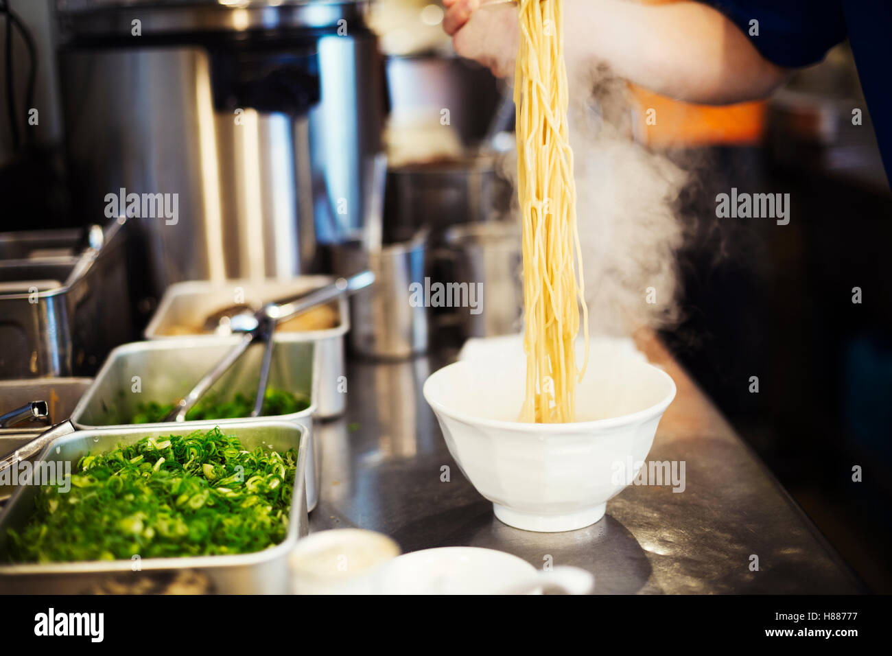 Un ramen noodle shop cucina. Uno chef che prepara le ciotole di spaghetti ramen in brodo, una specialità e fast food piatto. Foto Stock