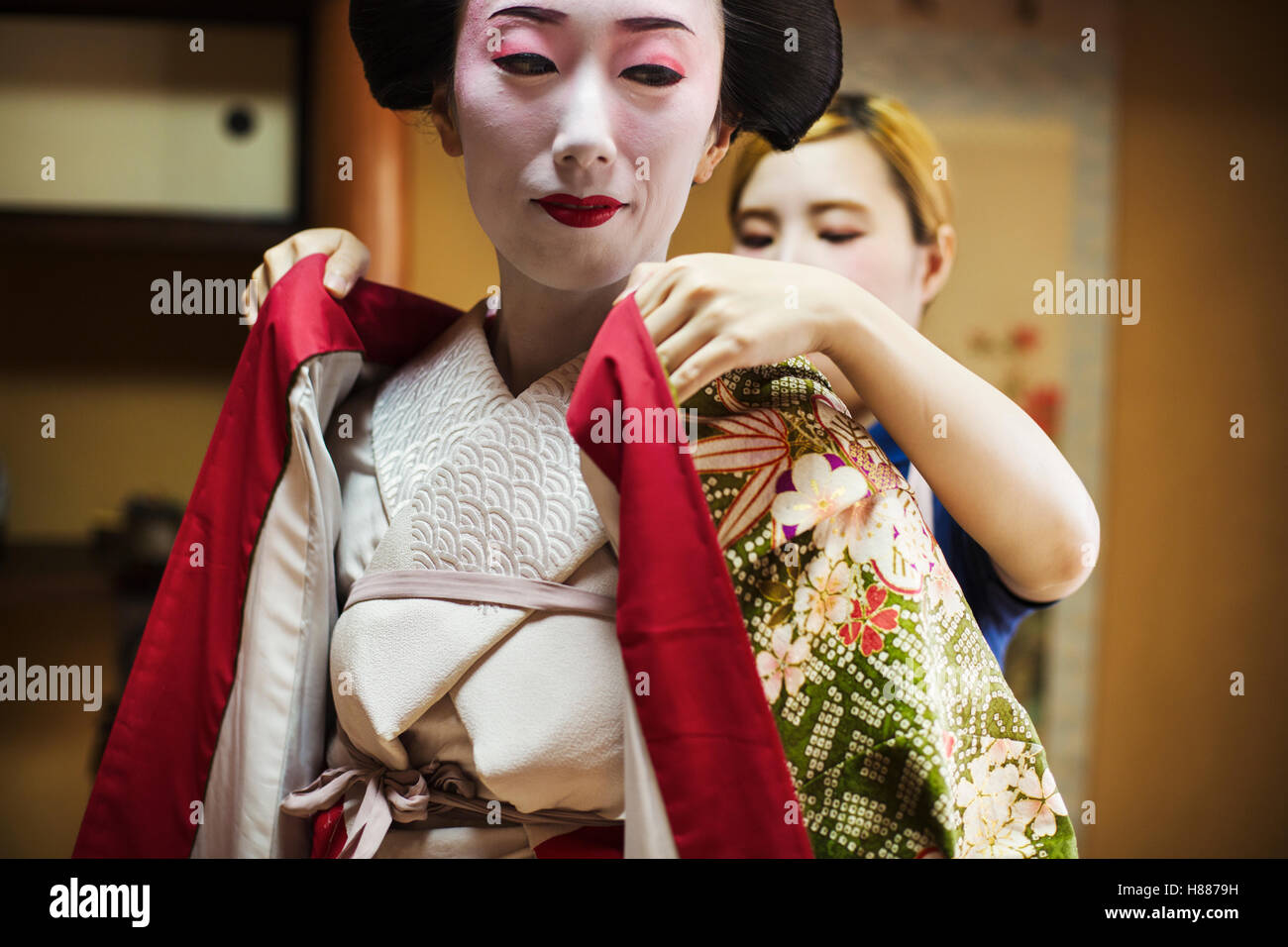 Una donna è vestita con il tradizionale stile geisha, indossando un kimono con faccia bianca di trucco con luminosi rossi labbra Foto Stock