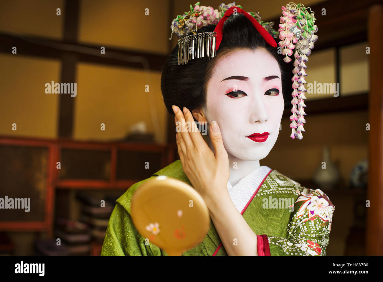 Una donna composta in tradizionale stile geisha, guardando in uno specchio a mano. Foto Stock