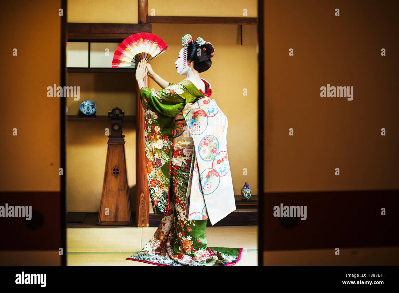 Una Donna vestita con il tradizionale stile geisha, indossando un kimono e OBI, in piedi in una posa classica con ventola sollevato Foto Stock
