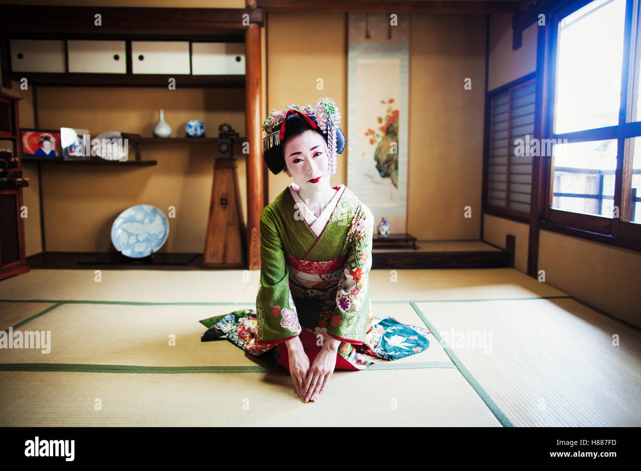 Una Donna vestita con il tradizionale stile geisha, indossando un kimono e OBI, inginocchiato in una posa tradizionale. Foto Stock