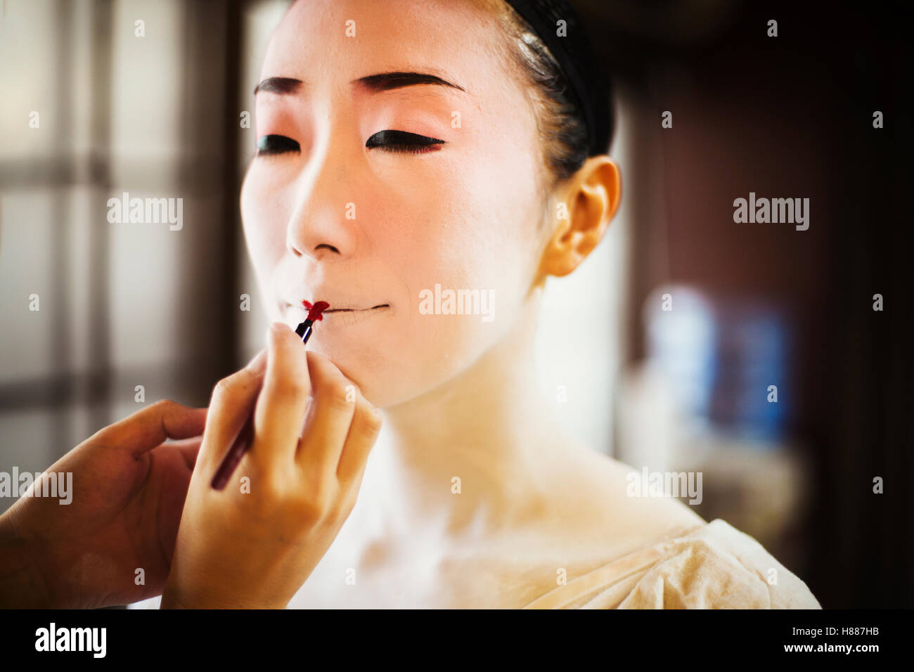 Una donna moderna creando il tradizionale geisha vivid red lips di pittura su rossetto con un pennello fine. White viso trucco. Foto Stock