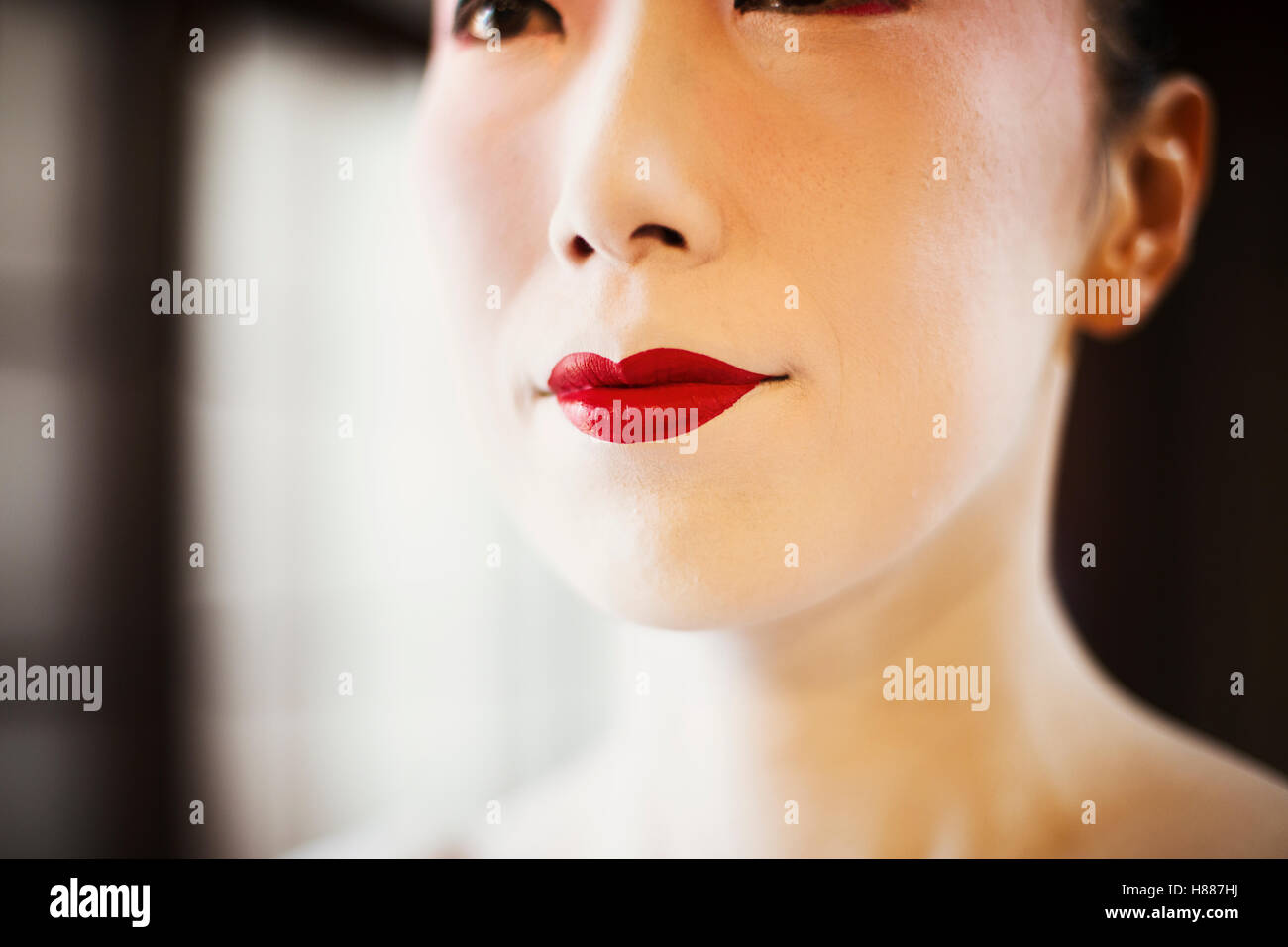 Una donna moderna creando il tradizionale geisha vivid red lips di pittura su rossetto con un pennello fine. White viso trucco. Foto Stock