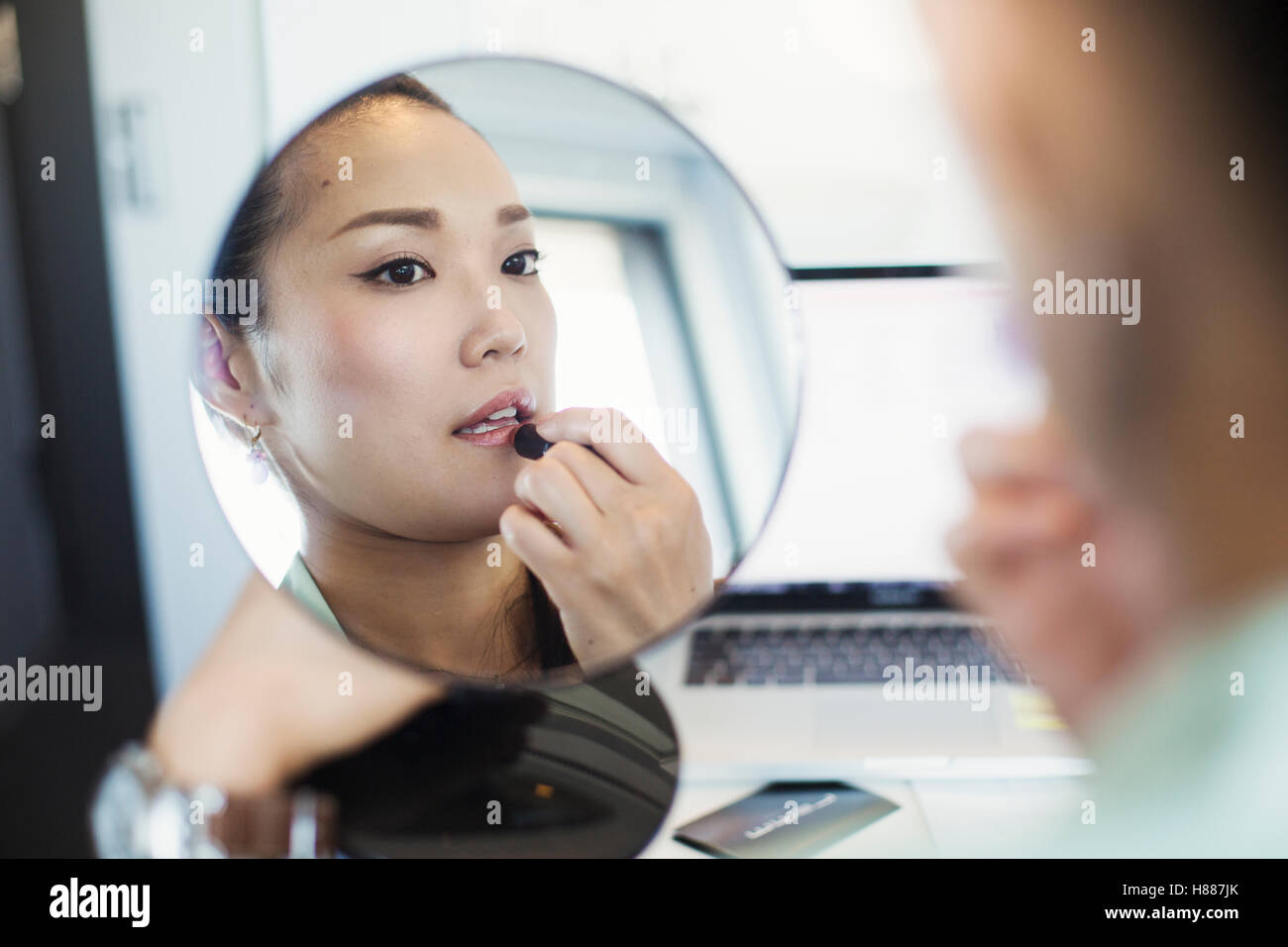 Una donna d'affari in preparazione per il lavoro, mettendo il rossetto e tenendo un mirror. Foto Stock
