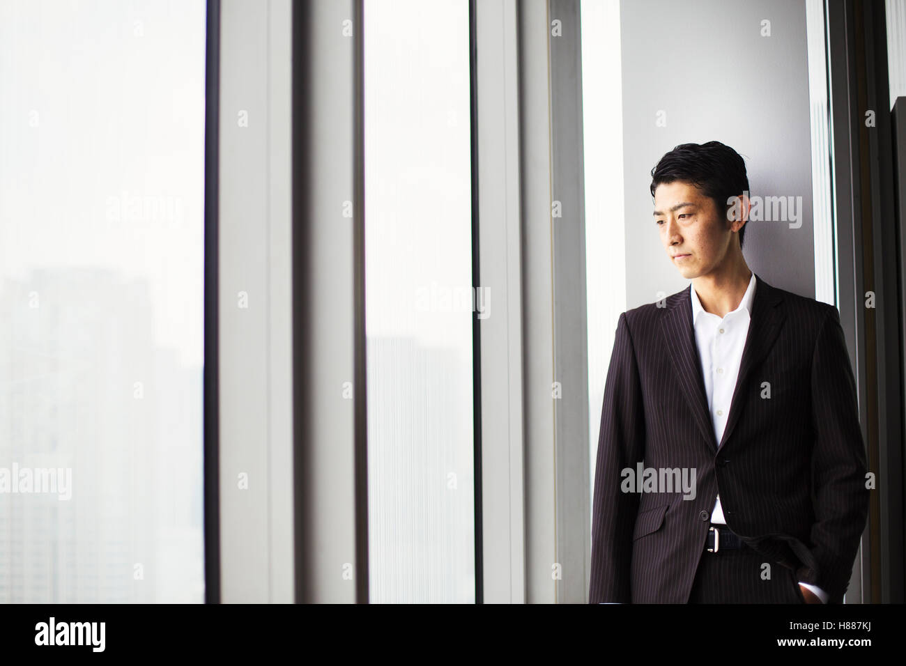 Un imprenditore in ufficio, da una grande finestra che si affaccia sulla città. Foto Stock