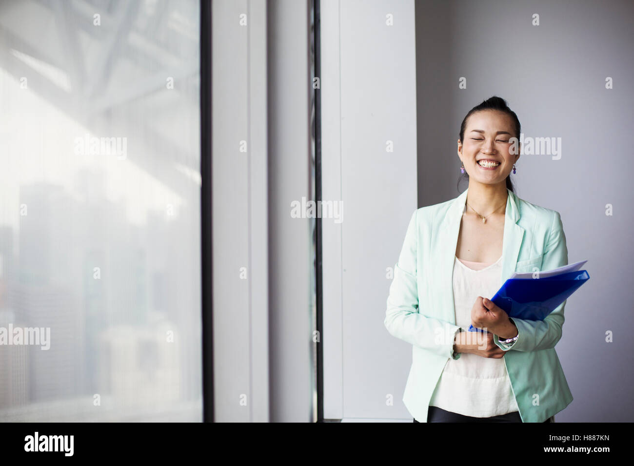 Una donna di affari in ufficio in possesso di una cartella e sorridente. Foto Stock
