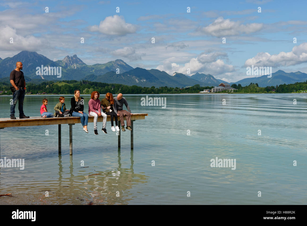 Famiglia seduta sul molo, Lago di Forggensee, Füssen Algovia, Baviera, Germania Foto Stock