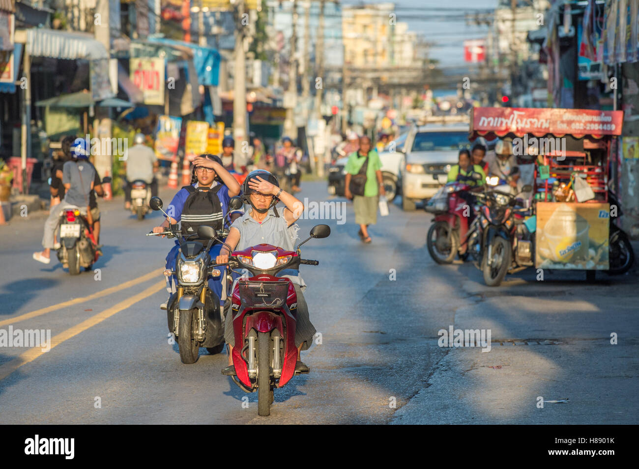 Persone guida a casa dal lavoro sulla moto su un tardo pomeriggio in Hua Hin, Thailandia Foto Stock