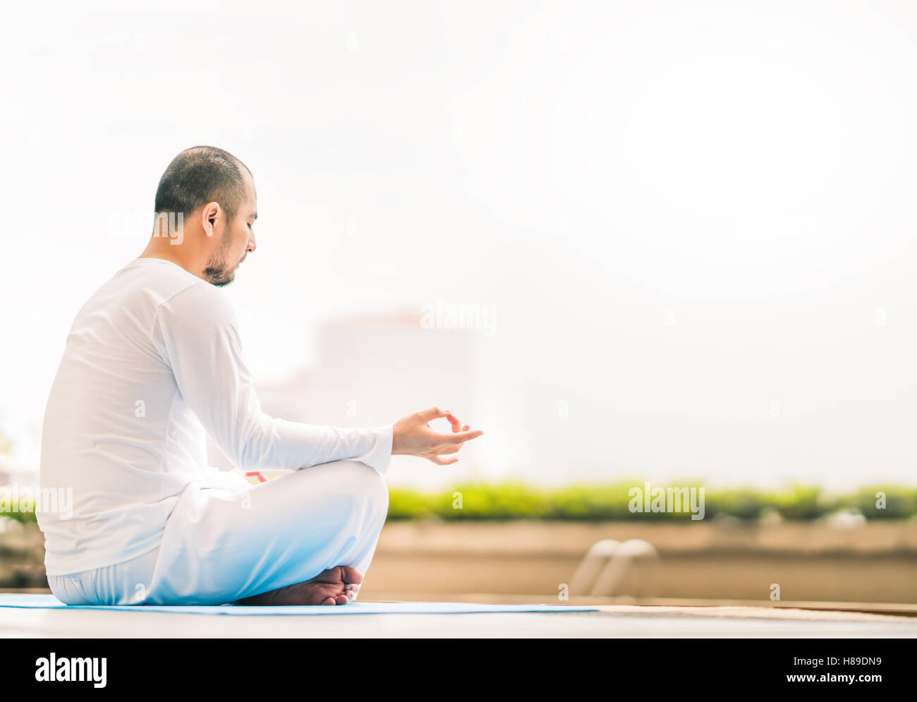 Giovane uomo meditando da piscina, yoga o rilassarsi concetto, vista città con sfondo spazio copia Foto Stock
