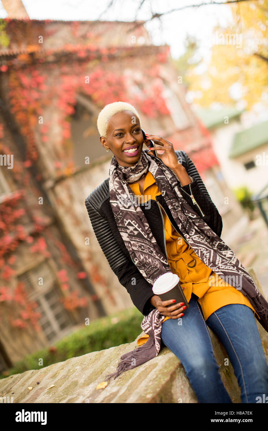 Piuttosto giovane donna nera con il telefono cellulare e la tazza di caffè Foto Stock