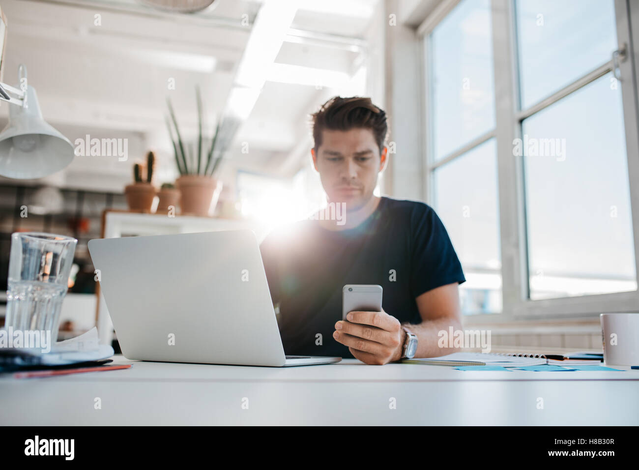 Colpo di giovane imprenditore la lettura di un messaggio di testo sul suo telefono cellulare mentre si lavora alla sua scrivania. Foto Stock