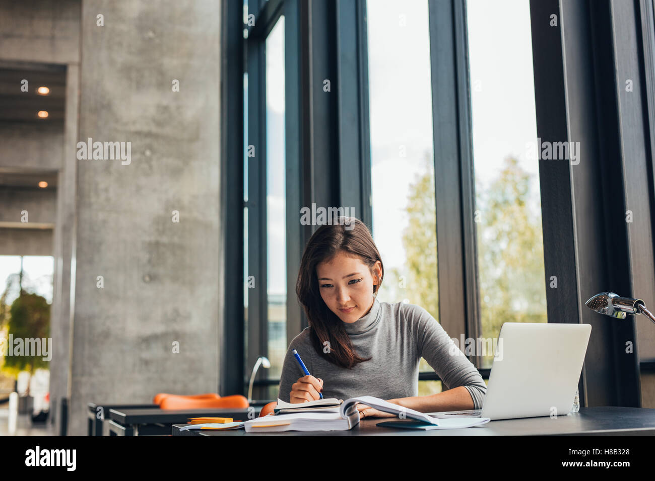 Giovane donna asiatica seduta a tavola con libri e computer portatile per la ricerca di informazioni. Giovane studentessa studiare in biblioteca. Foto Stock