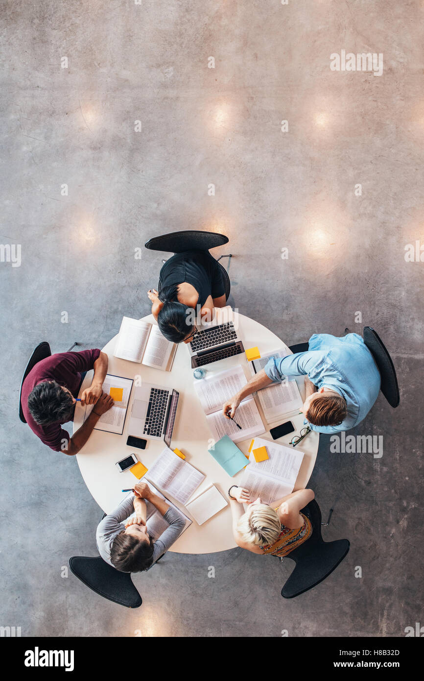 Gruppo di studenti che studiano insieme. Alta angolazione dei giovani seduti a tavola e a studiare con libri e laptop co Foto Stock