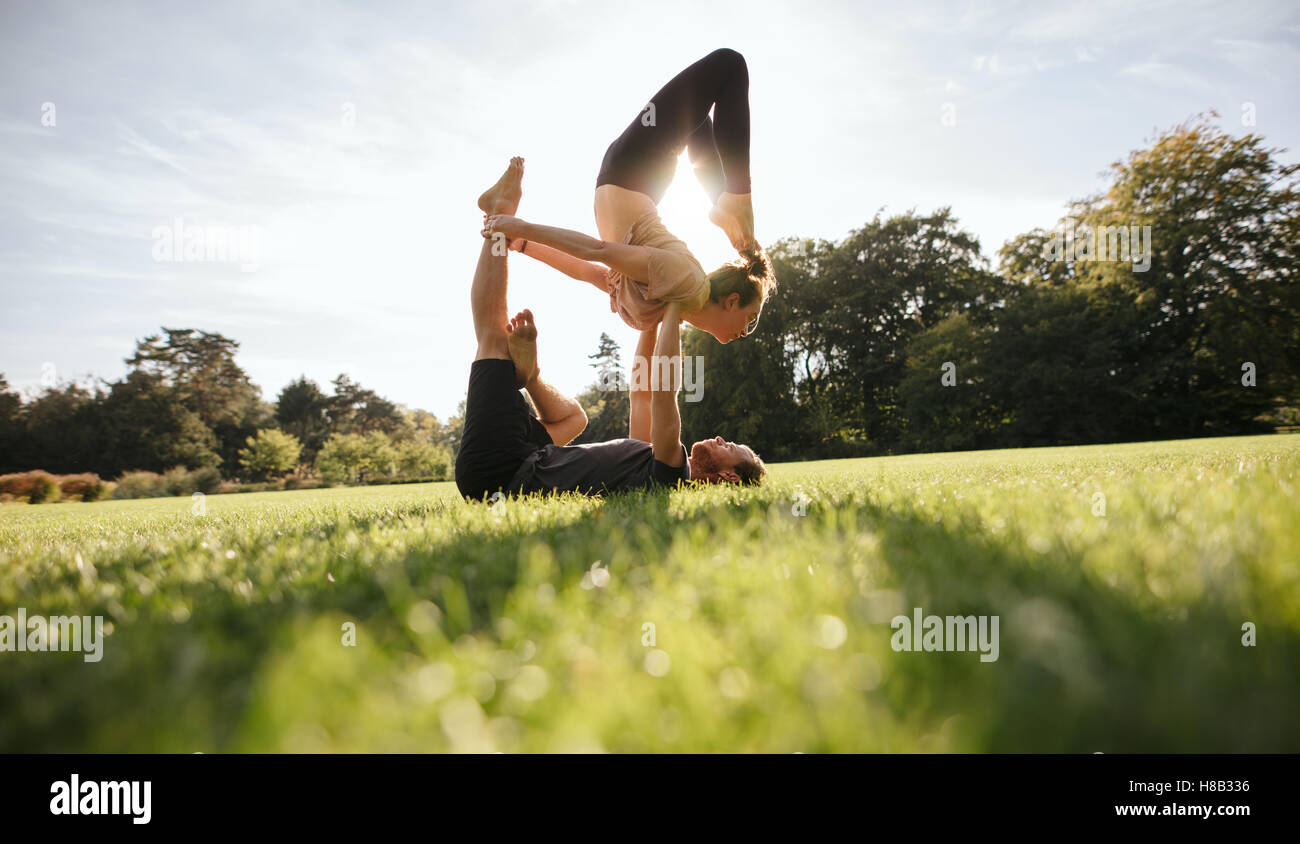 Colpo di coppia giovane facendo yoga acrobatico sul prato. Giovane uomo il sollevamento e il bilanciamento della donna al parco. Foto Stock