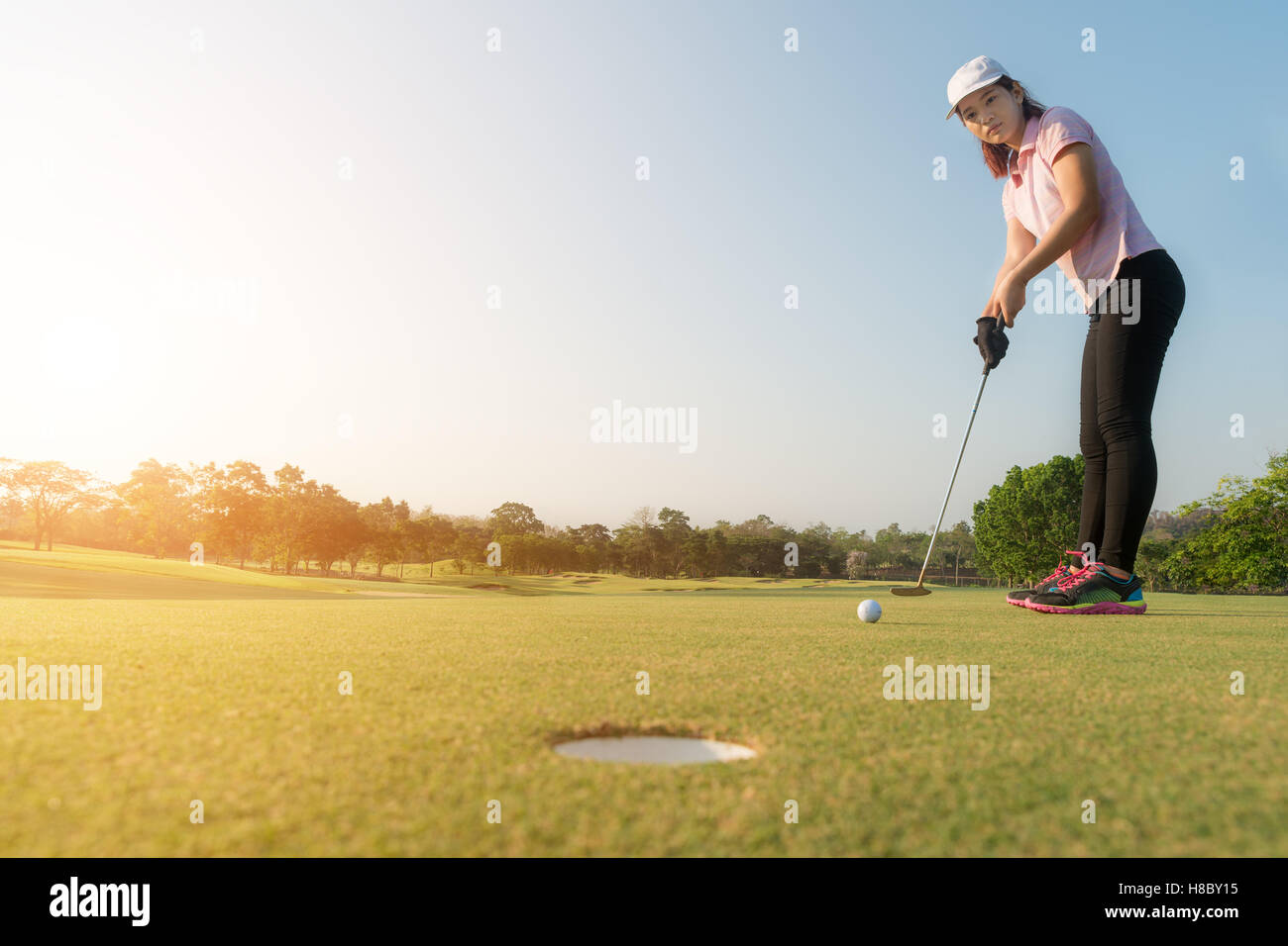 Donna asiatica giocatore di golf putting pallina da golf sul green, palla da golf cadere nel foro, cielo blu in background. Foto Stock