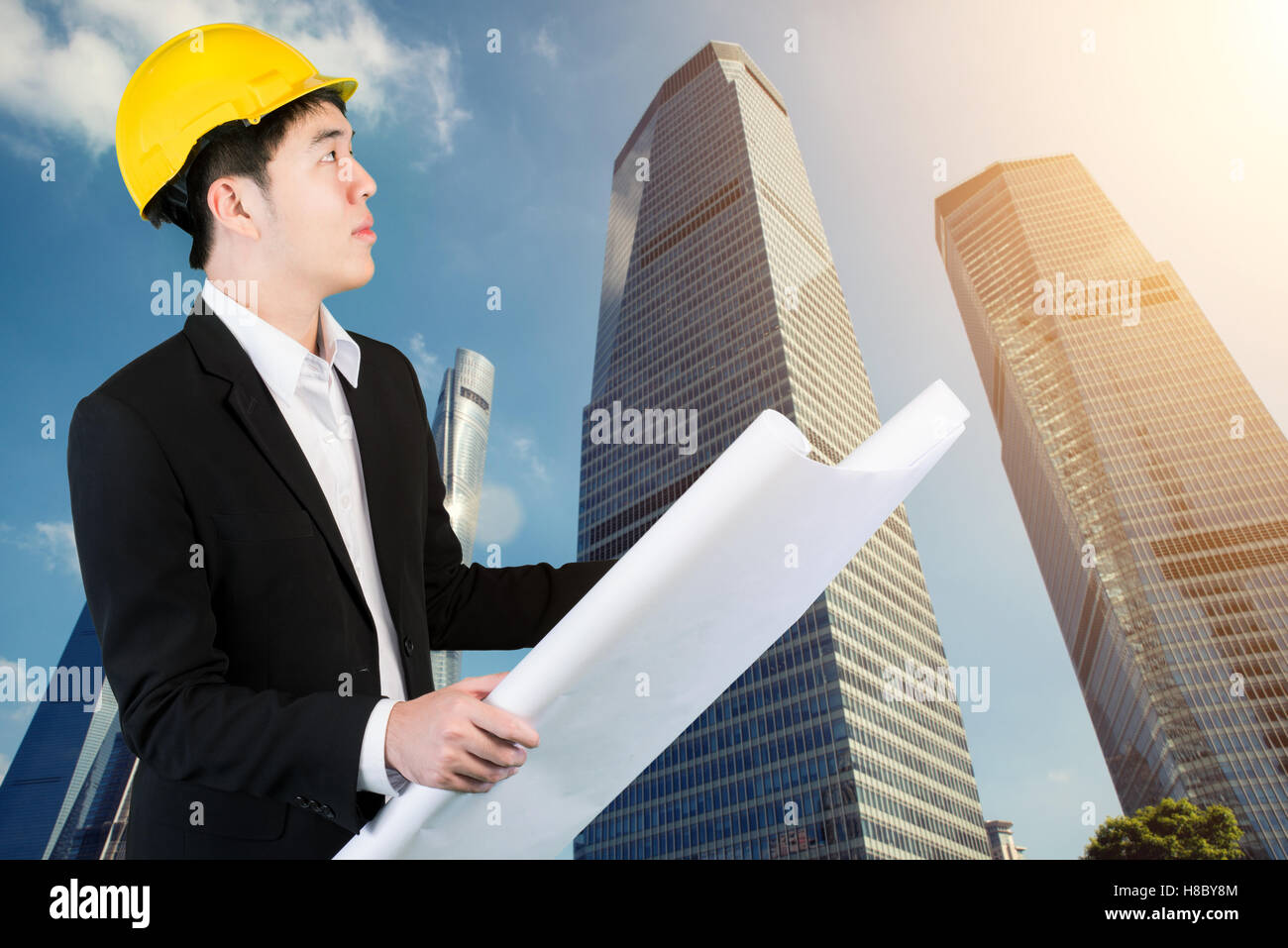 Ingegnere asiatici holding blueprint per la revisione del piano della città. Un alto e moderno grattacielo strutture in background Foto Stock