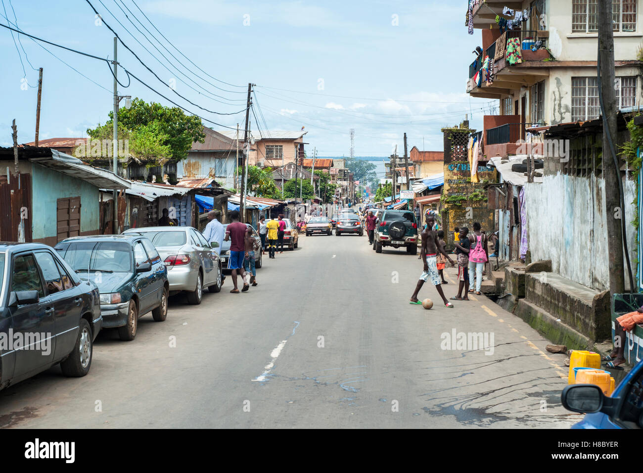 Una strada trafficata a Freetown con dei pedoni e dei veicoli parcheggiati ed edifici Foto Stock