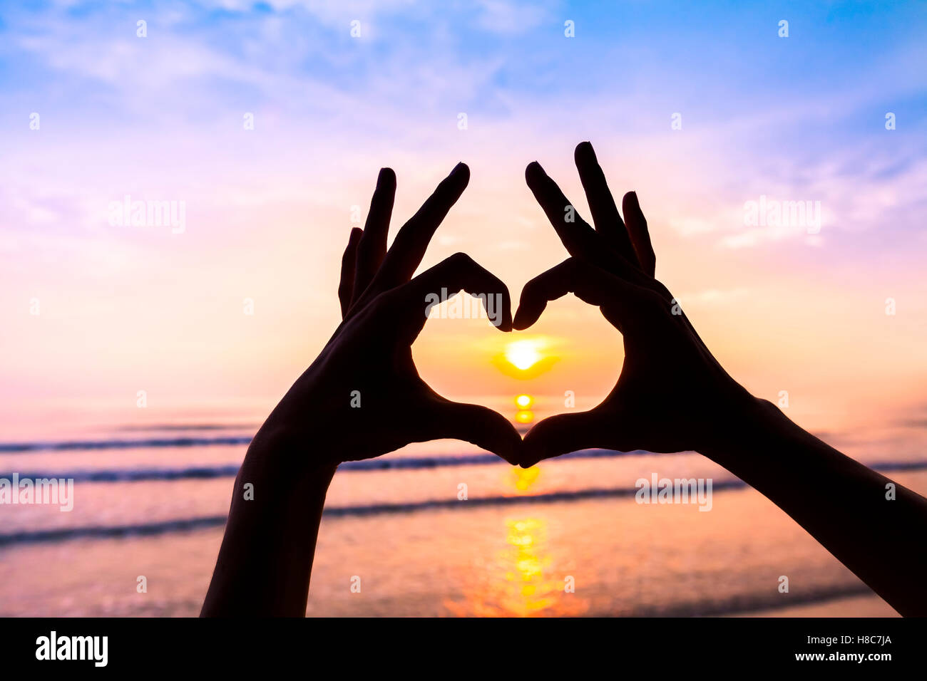 Donna con le mani in mano la creazione a forma di cuore con il tramonto sullo sfondo - simbolo di amore, romanticismo, amicizia, armonia Foto Stock