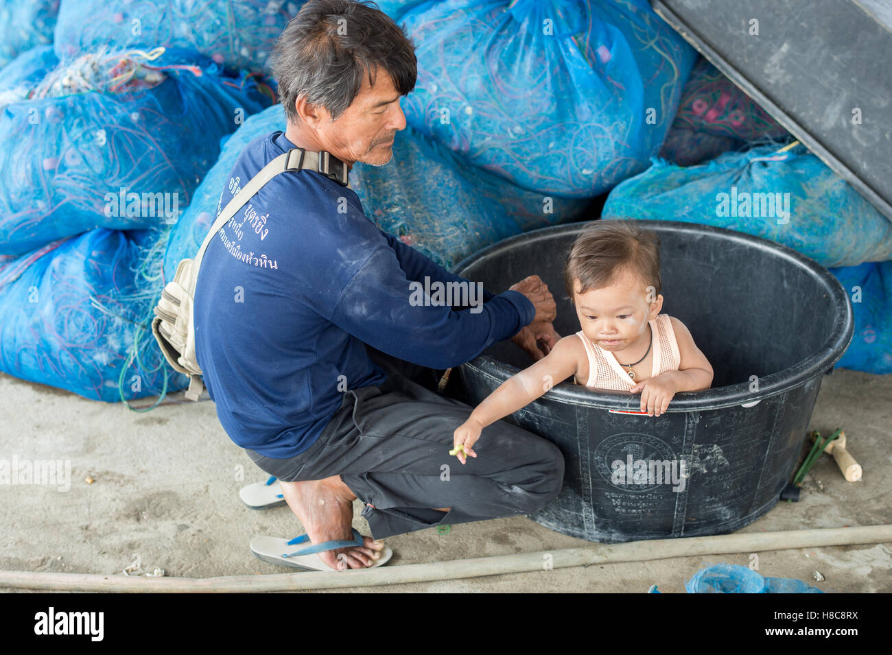 Thai l uomo si prende cura di un bambino durante la raccolta delle catture di frutti di mare dalla rete da pesca in un villaggio a sud di Hua Hin Foto Stock