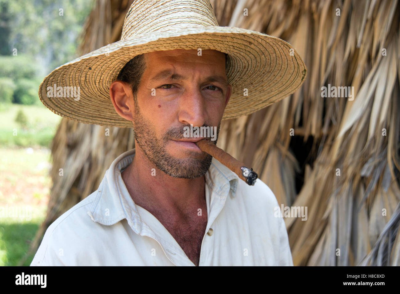 Ritratto di un agricoltore che indossa un cappello di paglia di fumare un sigaro con la paglia di essiccazione del tabacco casa sullo sfondo Vinales Cuba Foto Stock