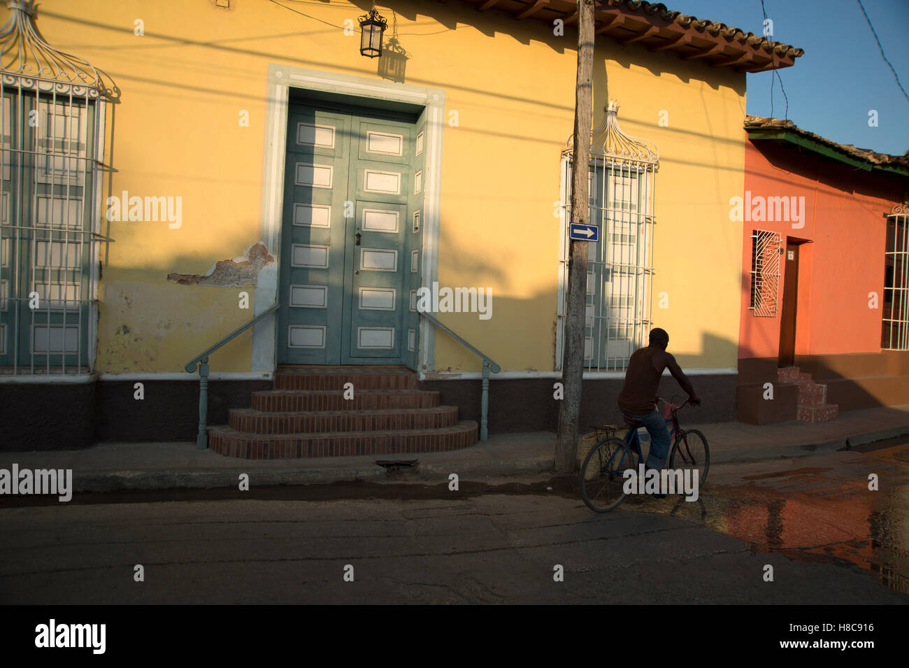 Un uomo cubano corse in bicicletta il suo passato qualche dipinto luminosamente case come il sole scende in Trinidad, Cuba Foto Stock