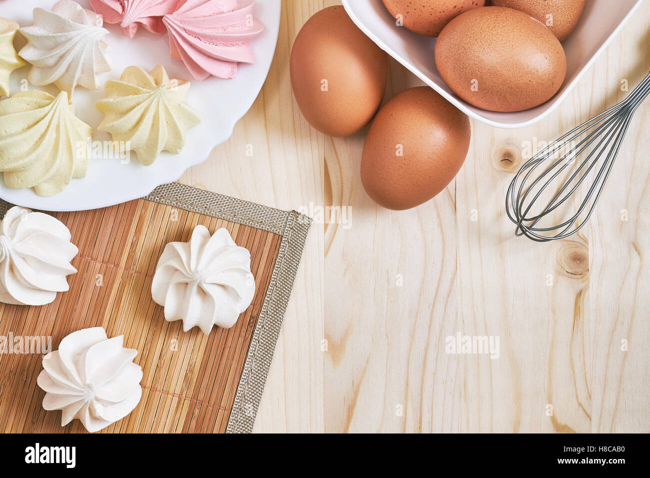 Freschi colori deliziosi biscotti di meringa su un tavolo di legno con le uova e mescolare con una frusta. Vista da sopra con lo spazio di copia Foto Stock