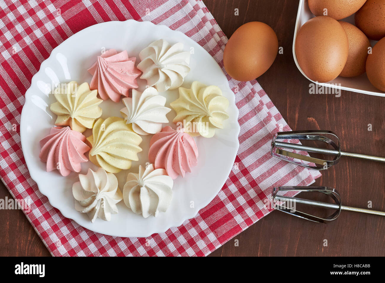 Freschi colori deliziosi biscotti meringa servita su piastra bianca con uova e miscelatore. Vista superiore Foto Stock