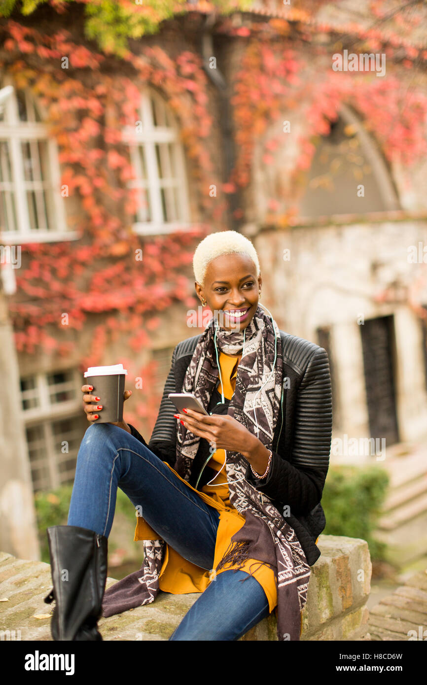 Moderno e giovane africano donna americana in posa con caffè di andare e il telefono cellulare all'aperto Foto Stock
