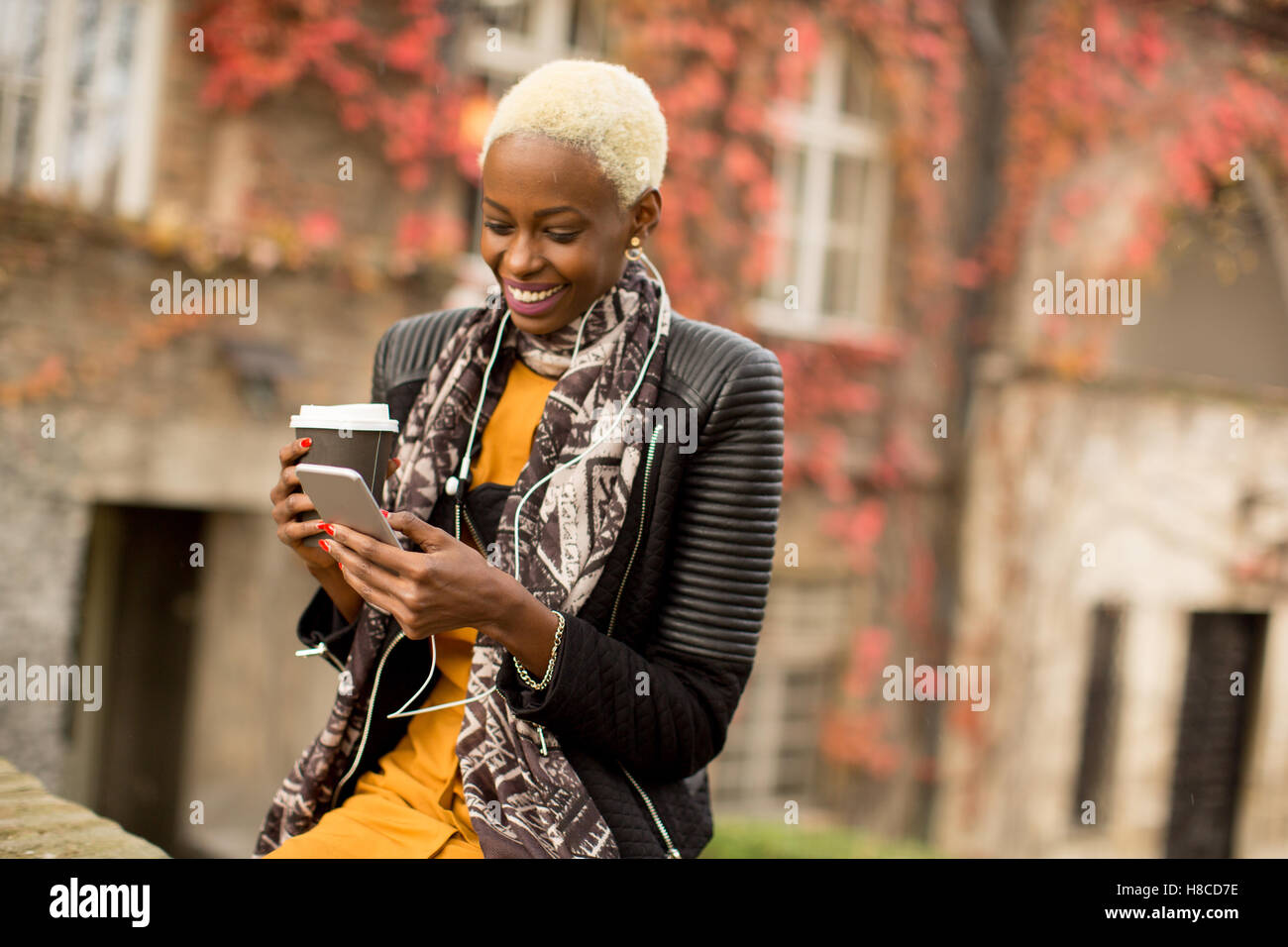 Moderno e giovane africano donna americana in posa con caffè di andare e il telefono cellulare all'aperto Foto Stock