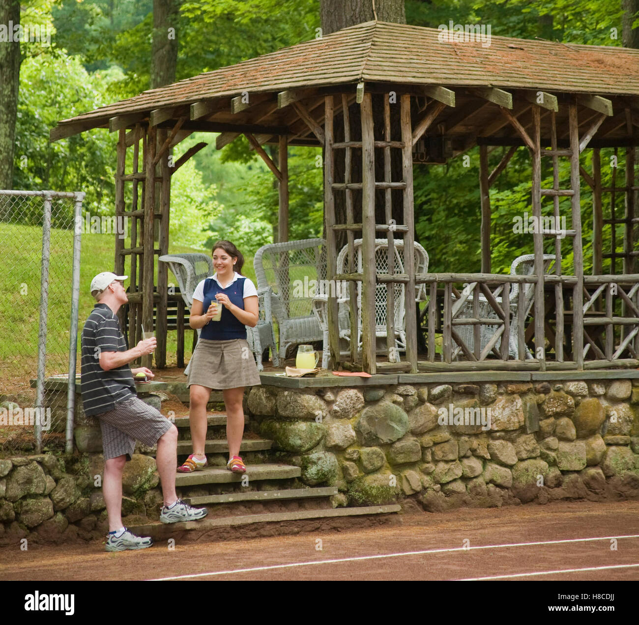 Due persone che parlano sui gradini che portano al legno casa estiva accanto al campo da tennis in argilla rossa. Foto Stock
