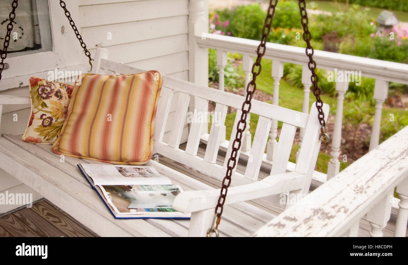 Cuscino e libro sul sedile oscillante sulla veranda. Foto Stock