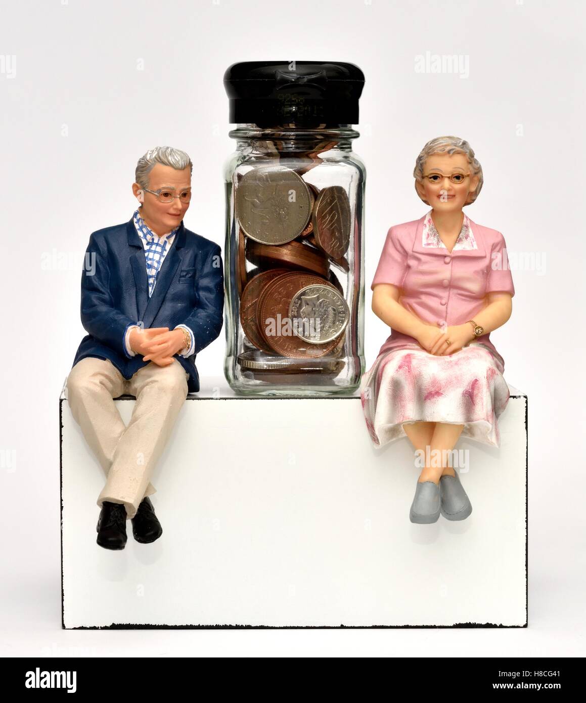 Titolare di una pensione o di una rendita figurina giovane seduto con monete in un piccolo vaso in vetro. Foto Stock