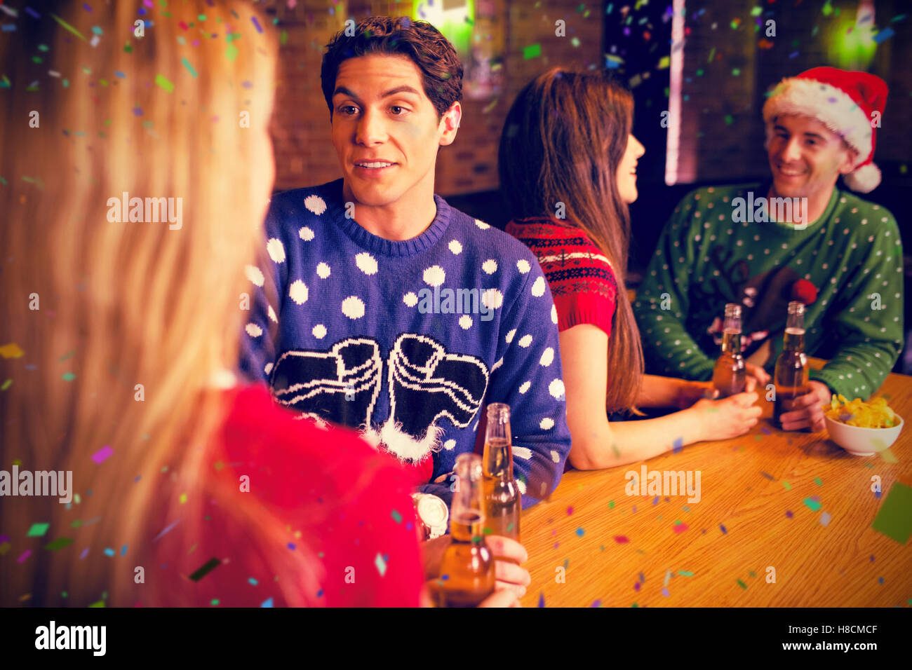 Immagine composita di amici avente birre dalla tavola durante il periodo di Natale Foto Stock