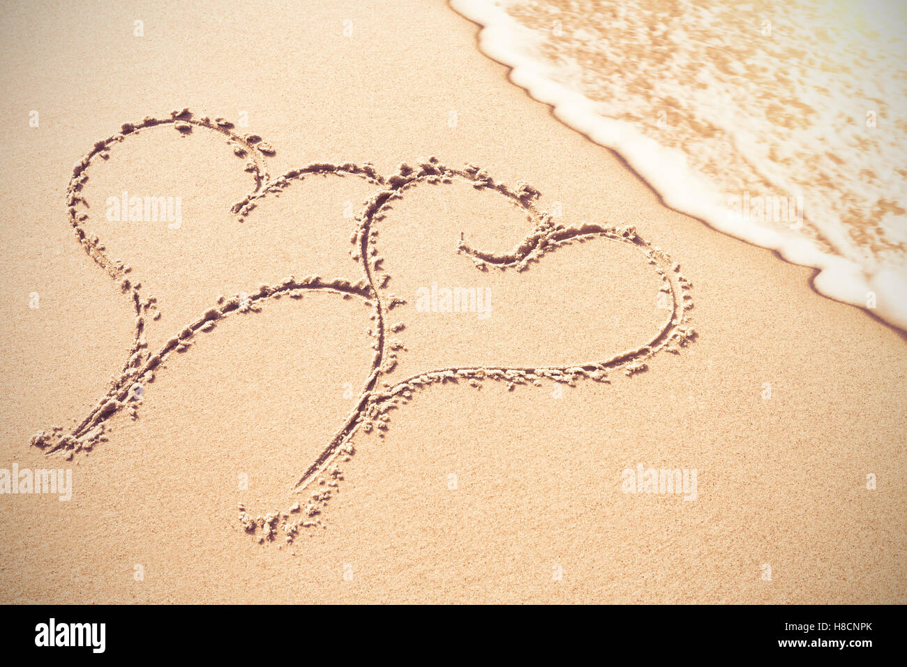 Due forme di cuore inscrivere sulla sabbia Foto Stock