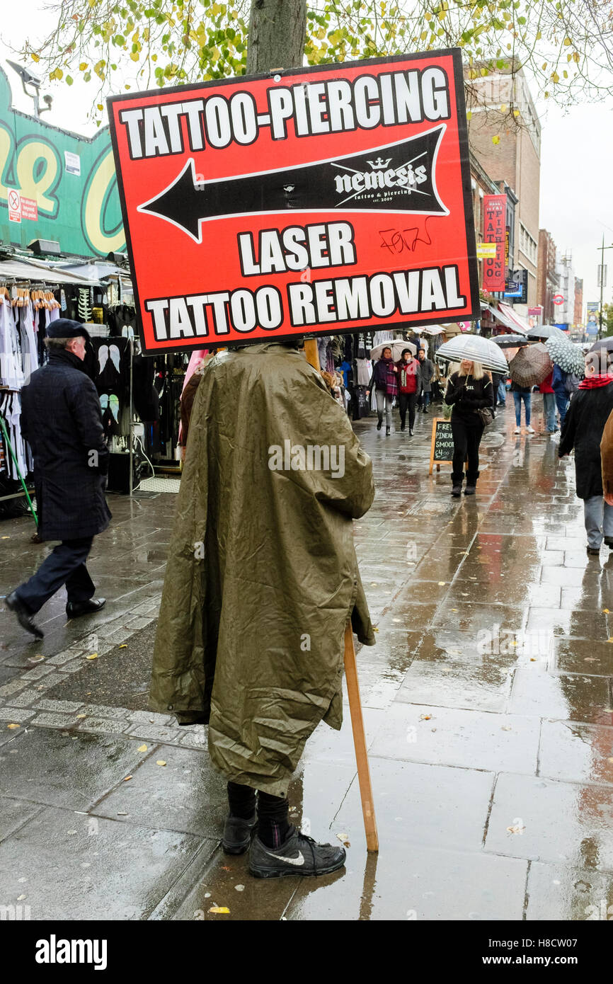 Persona in possesso di segno pubblicità tatuaggi, piercing e tatuaggio servizi di rimozione, Camden High Street, Londra, Regno Unito. Foto Stock