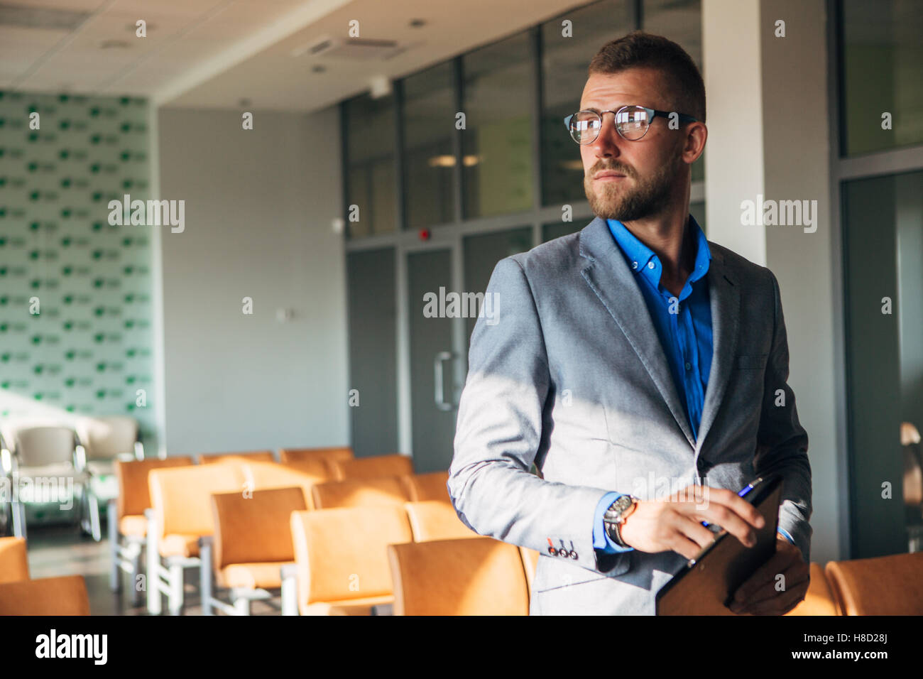 Imprenditore elegante in giacca e occhiali guarda fuori dalla finestra Foto Stock