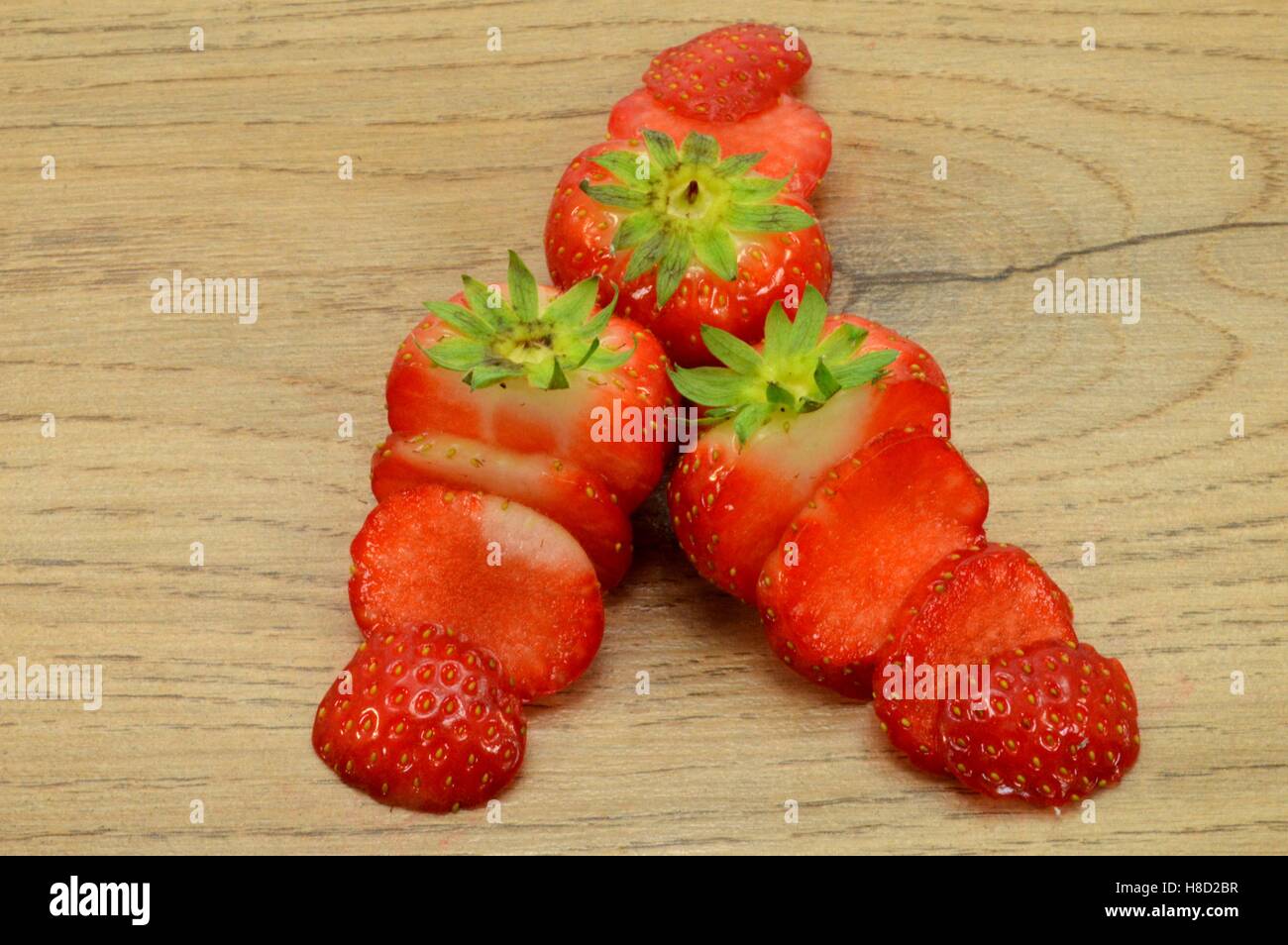 Il trio di fragole tagliate in strisce su una luce sullo sfondo di legno Foto Stock