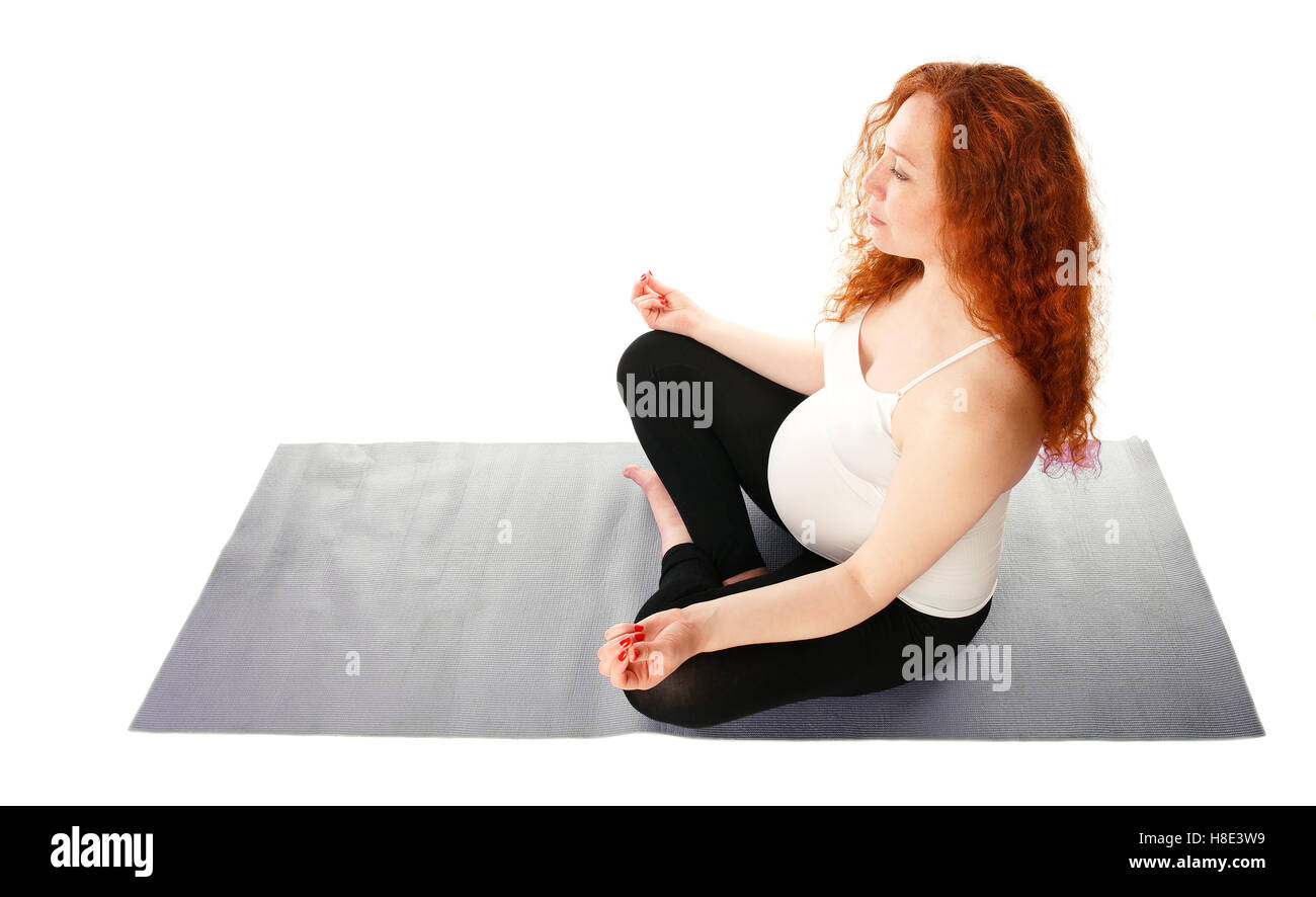 Donna incinta seduta con le gambe incrociate e fare yoga. Isolato su bianco. Foto Stock