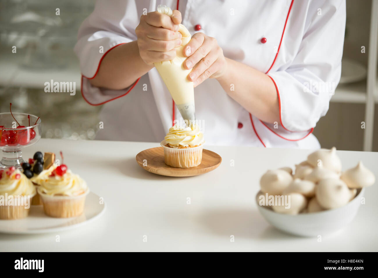 Close up di mani topping una tortina con crema Foto Stock