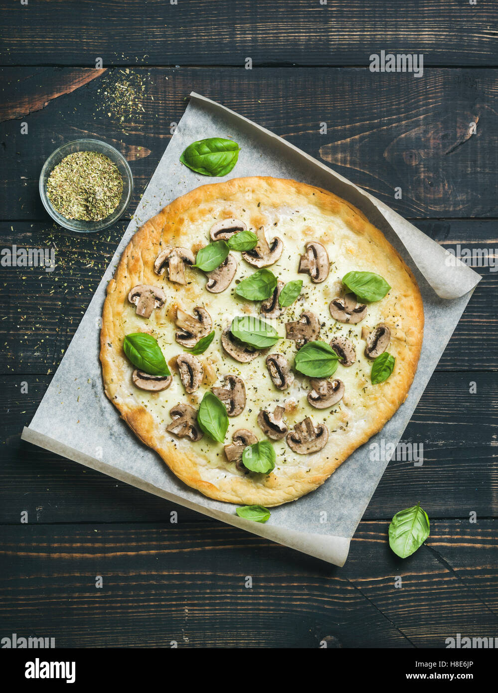 In casa la pizza a fungo con le foglie di basilico e spezie in vetro su carta da forno più scuri in legno bruciata sfondo, vista dall'alto, ve Foto Stock