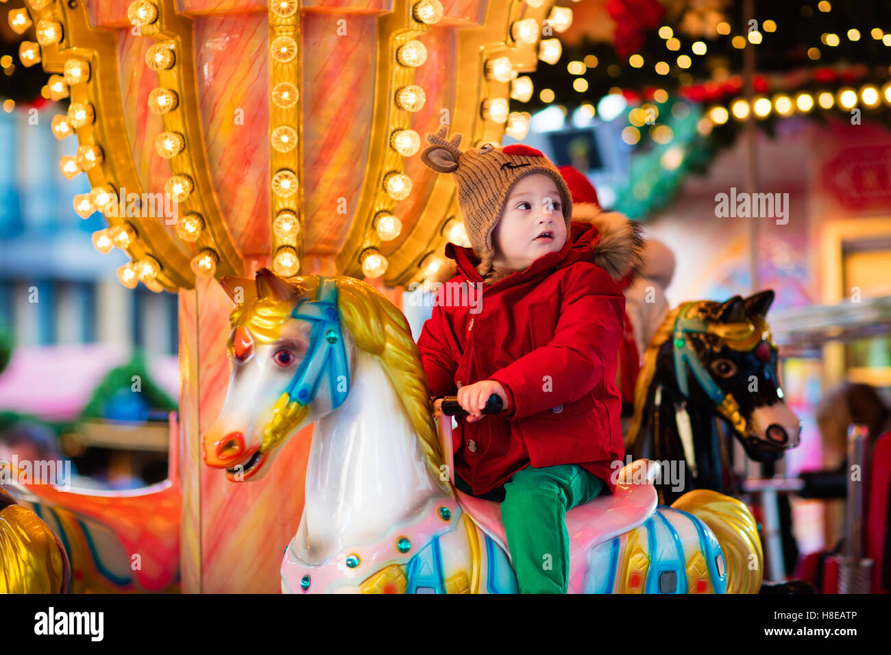 Happy little boy in una giacca calda e maglia rossa Nordic cappello e sciarpa giostra di equitazione cavallo durante il viaggio in famiglia Foto Stock