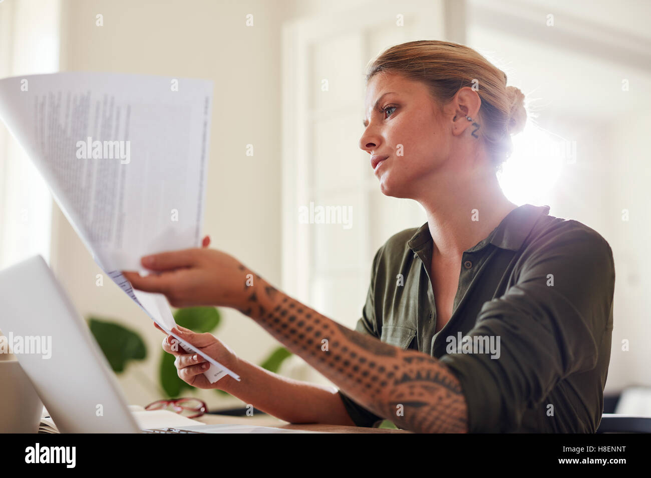 Ritratto di giovane e bella donna seduta al tavolo e la lettura dei documenti. Andando femmina attraverso alcune pratiche a casa. Foto Stock
