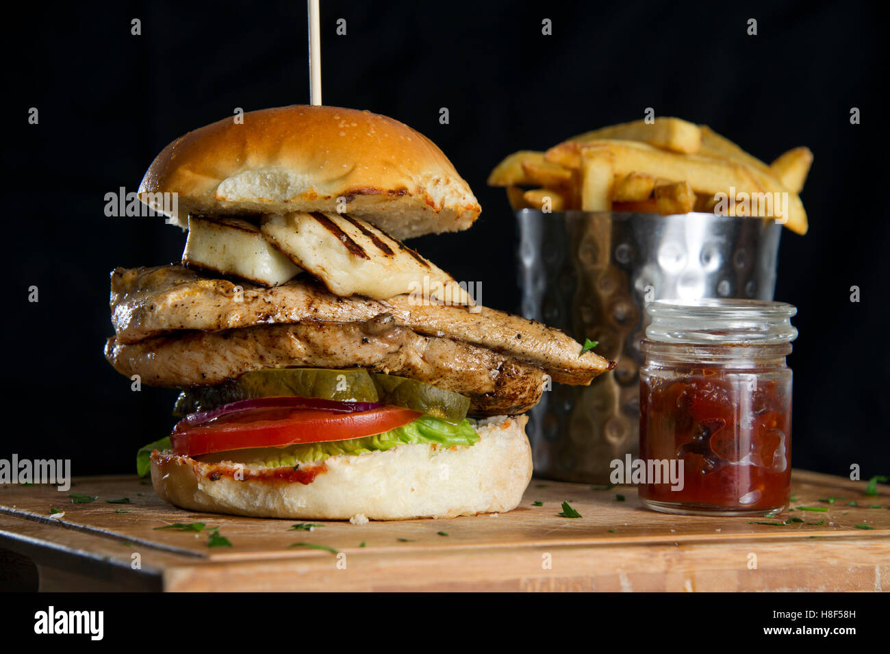 Un hamburger di pollo con patatine (patatine fritte) su un tagliere di legno. un cibo DEL REGNO UNITO Foto Stock