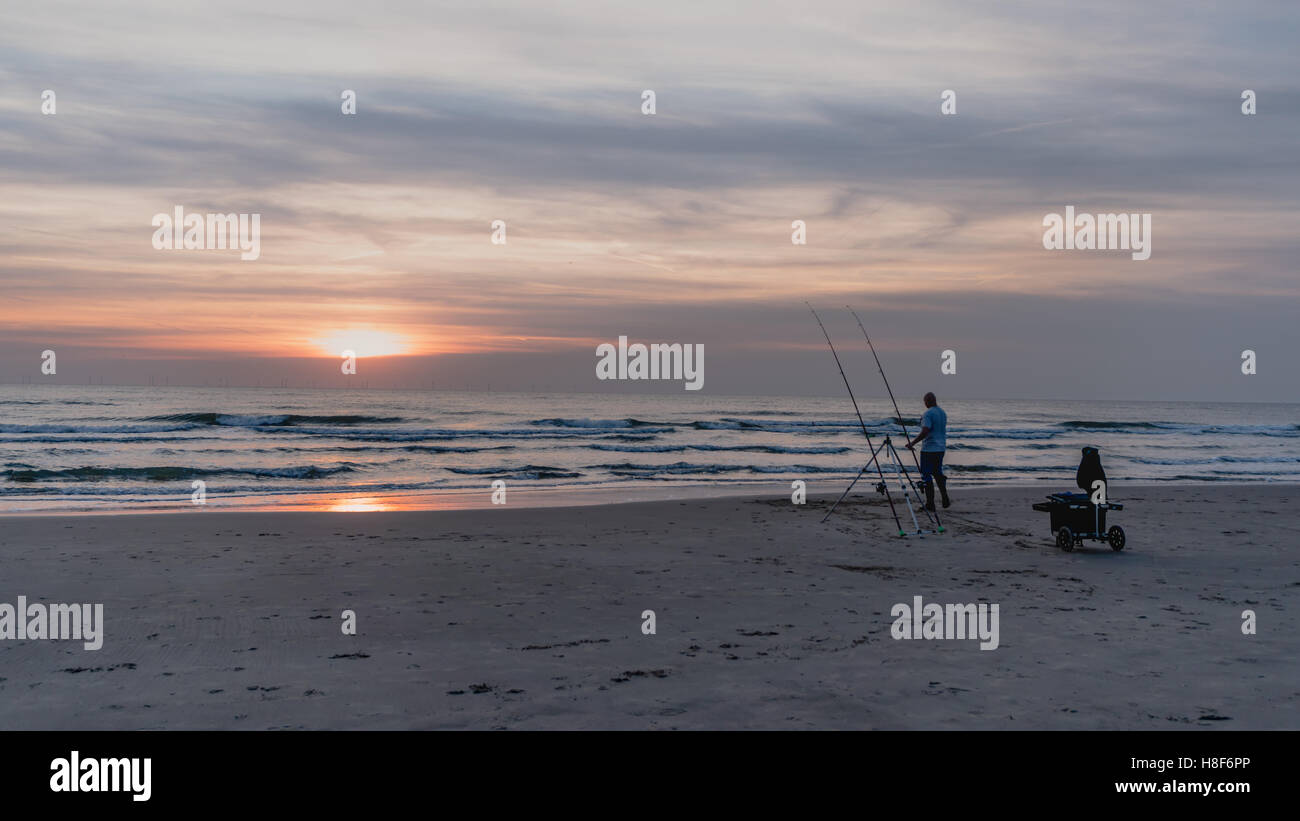 La pesca con lenza in mare pescatore al tramonto presso la spiaggia del Mare del Nord in Egmond aan Zee, Paesi Bassi Olanda Settentrionale Foto Stock