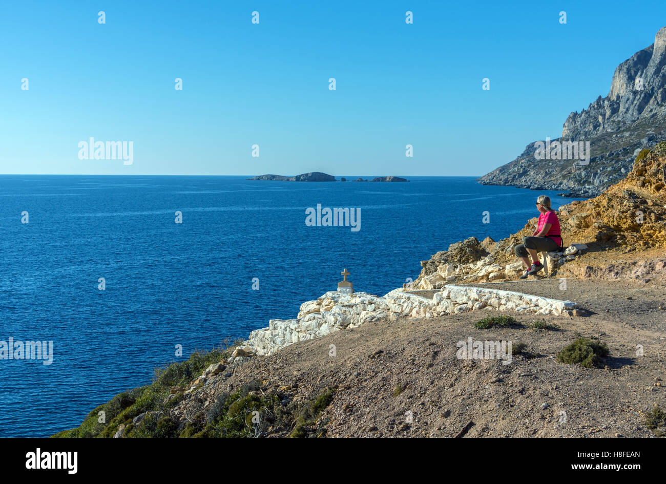 Femmina in rosso sat da passi che si affaccia sul mare, Telendos Grecia Foto Stock