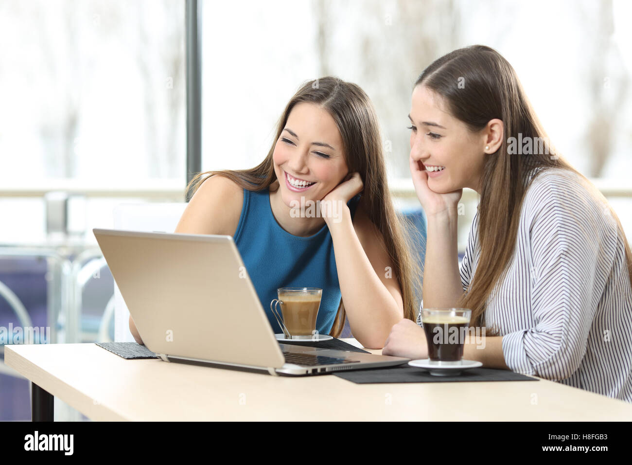Due felici donne gli amici a guardare i contenuti multimediali in linea in un computer portatile seduti in un caffè Foto Stock