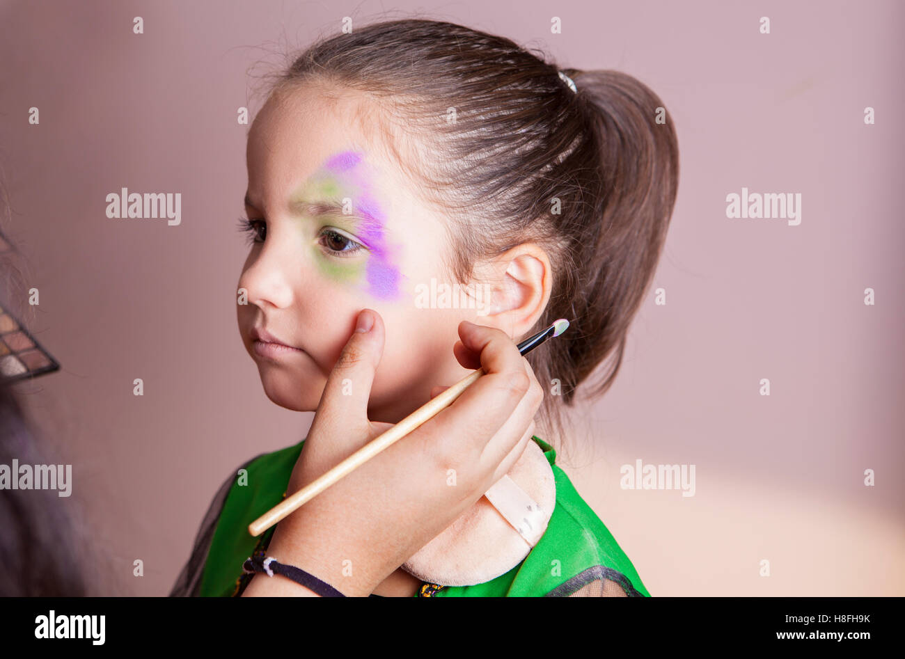 Poco carino ragazza rendendo facepaint prima festa di Halloween. Il make-up artist è di applicare alcuni dei colori Foto Stock