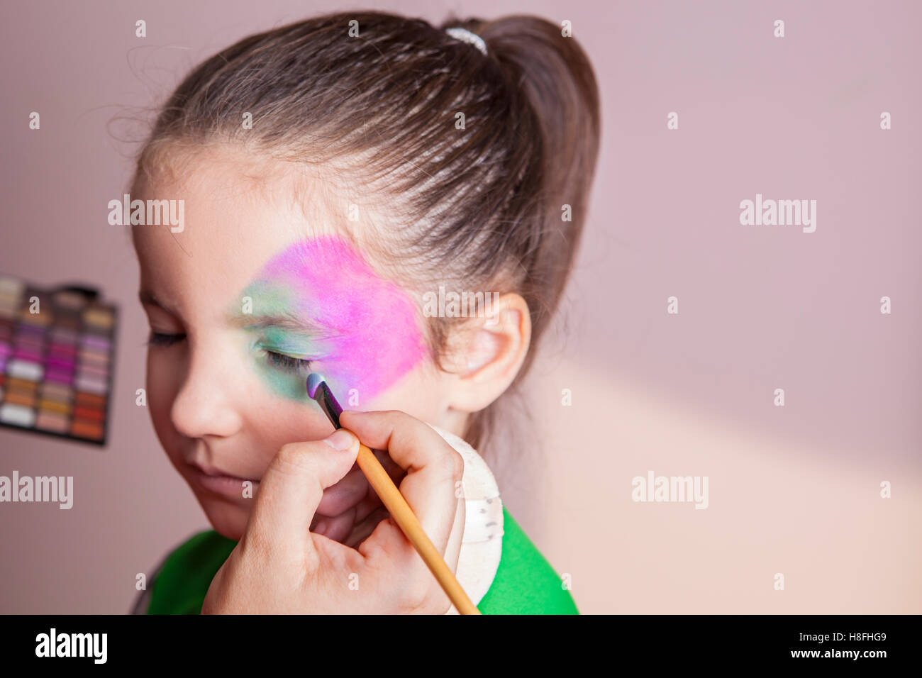 Poco carino ragazza rendendo facepaint prima festa di Halloween. Il make-up artist è di applicare alcuni dei colori Foto Stock