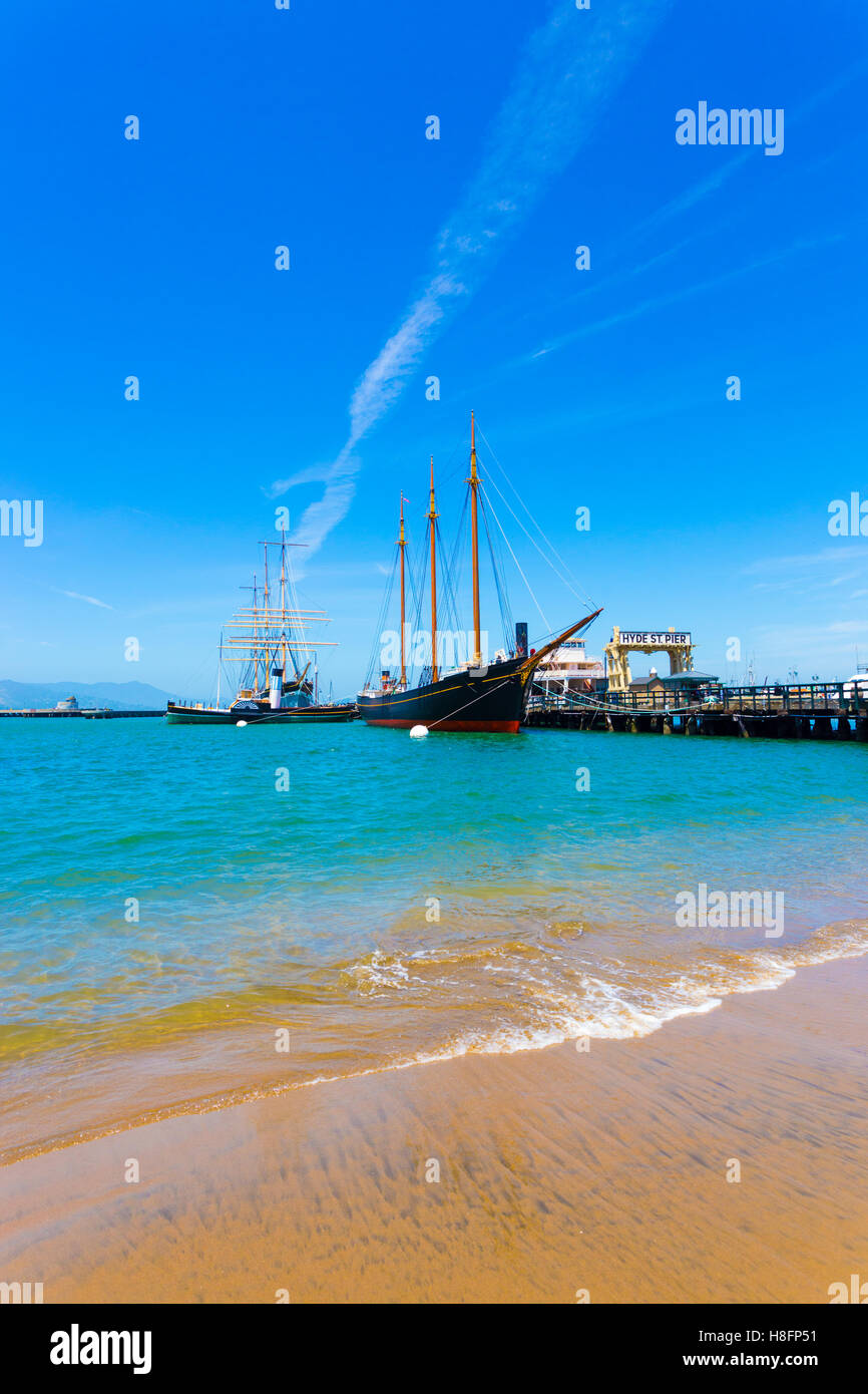 Ampia angolazione del primo piano sulla spiaggia accanto al Hyde Street Pier attrazione turistica con le navi al Pontile del Pescatore su un estate Foto Stock