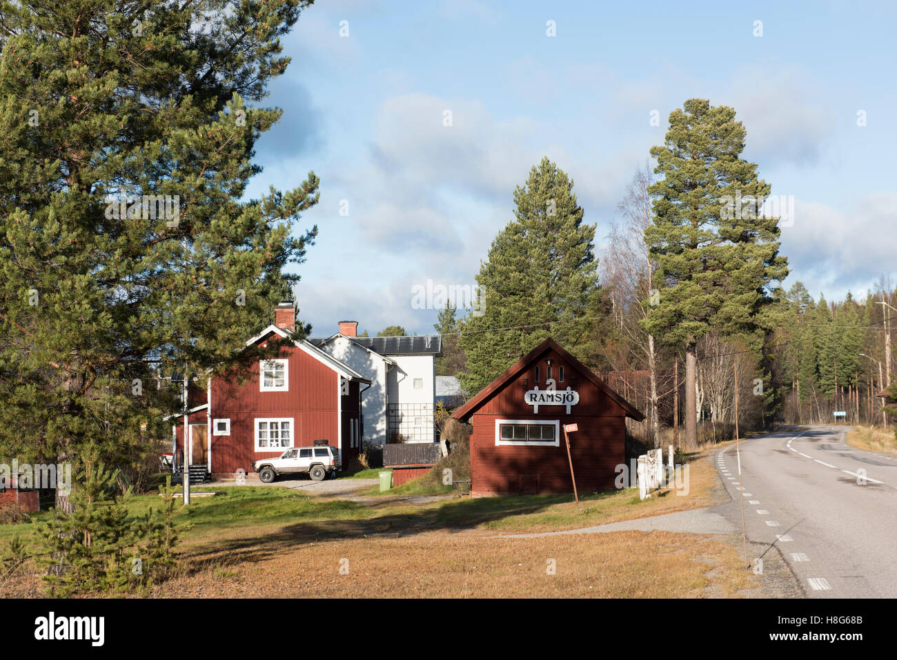 Villaggio rurale svedese con case di legno rosse, pini e una strada tranquilla che si snoda attraverso il paesaggio in una luminosa giornata autunnale. Foto Stock